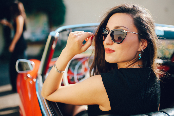 A lady in a convertible wearing sunglasses looks back at the camera