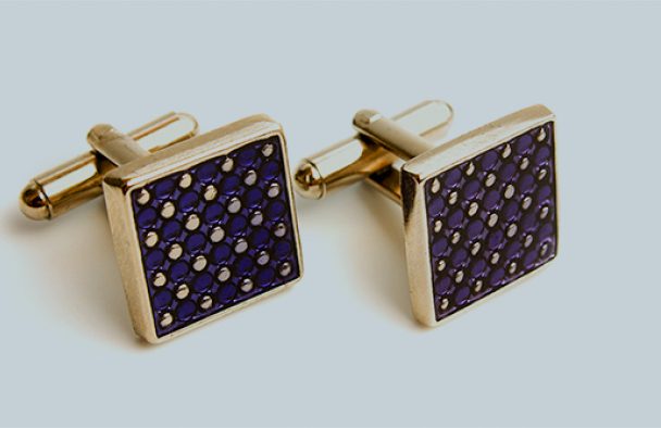 A pair of gold and blue cuff links on display with a grey background.