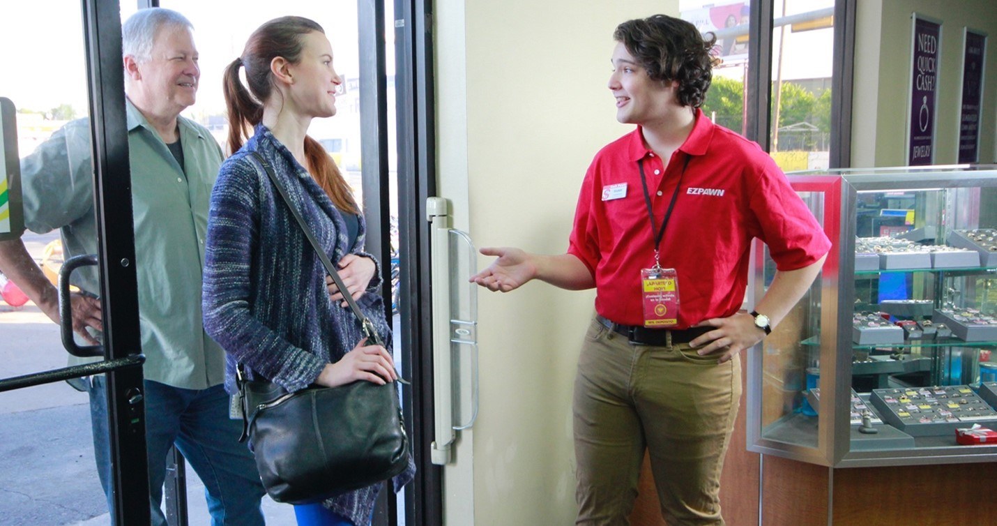 EZPAWN employee greets two customers at the front door.