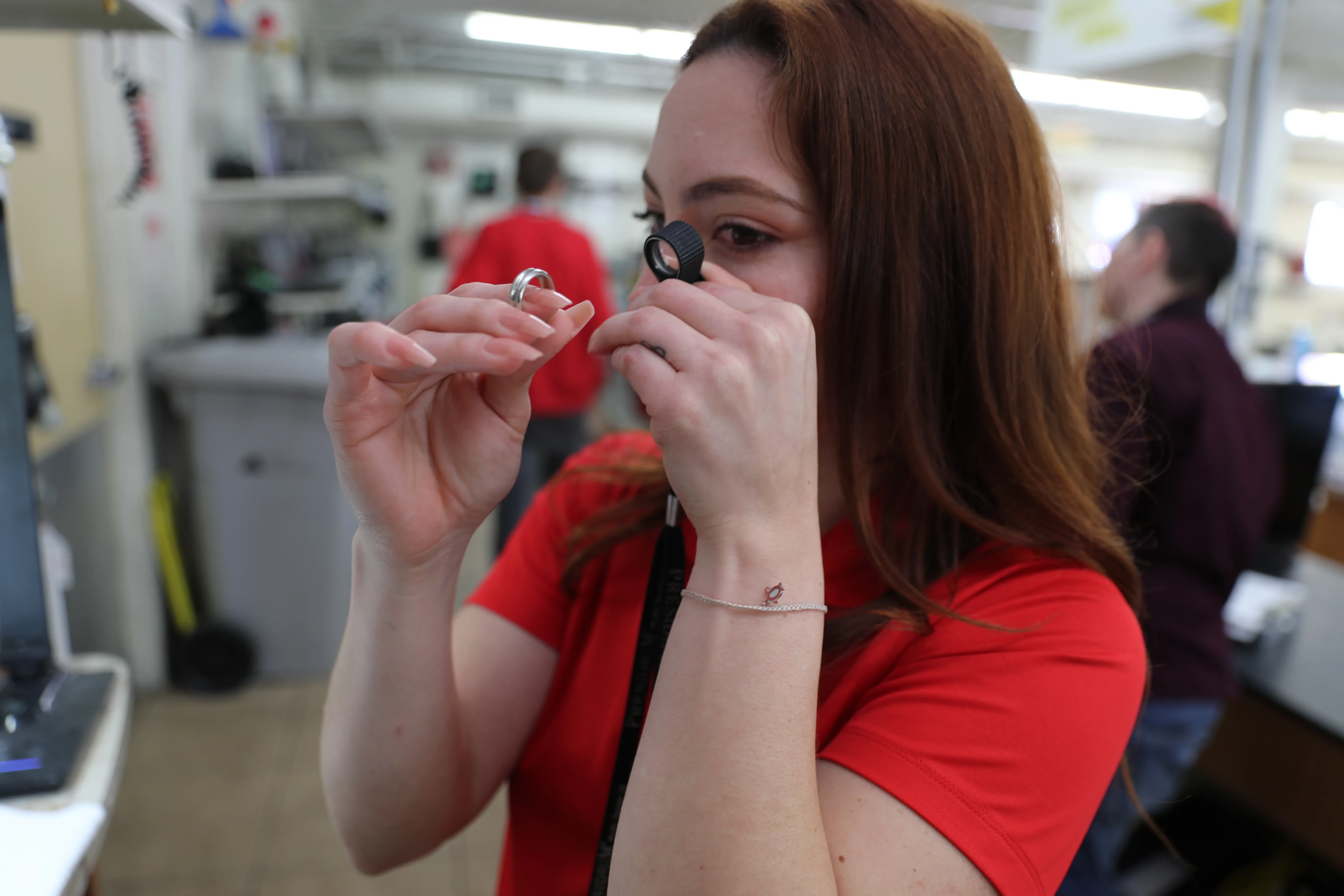 A team member is inspecting a diamond ring through a glass eye piece in the back of the store.