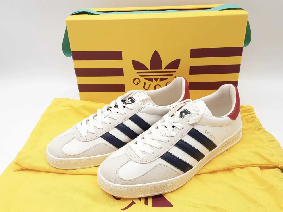 Adidas Gazelle sneakers in white with navy blue stripes and a hint of red on the heel, along with their branded box.