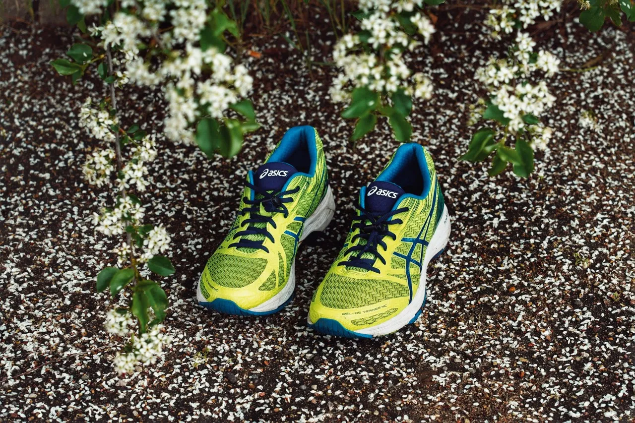 A pair of bright green and blue Asics running shoes placed outdoors among flowers.