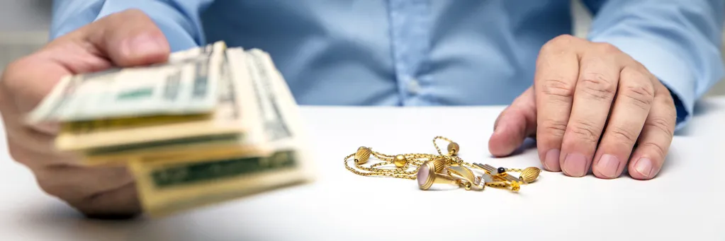 A man holding out cash with gold jewelry on the coutner.