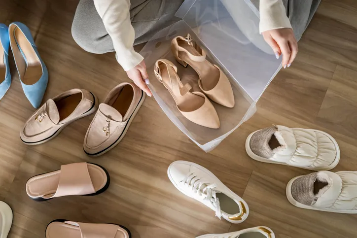 A variety of shoes spread out on the floor, including slippers, loafers, sandals, and sneakers. The image appears to show someone organizing or packing shoes.