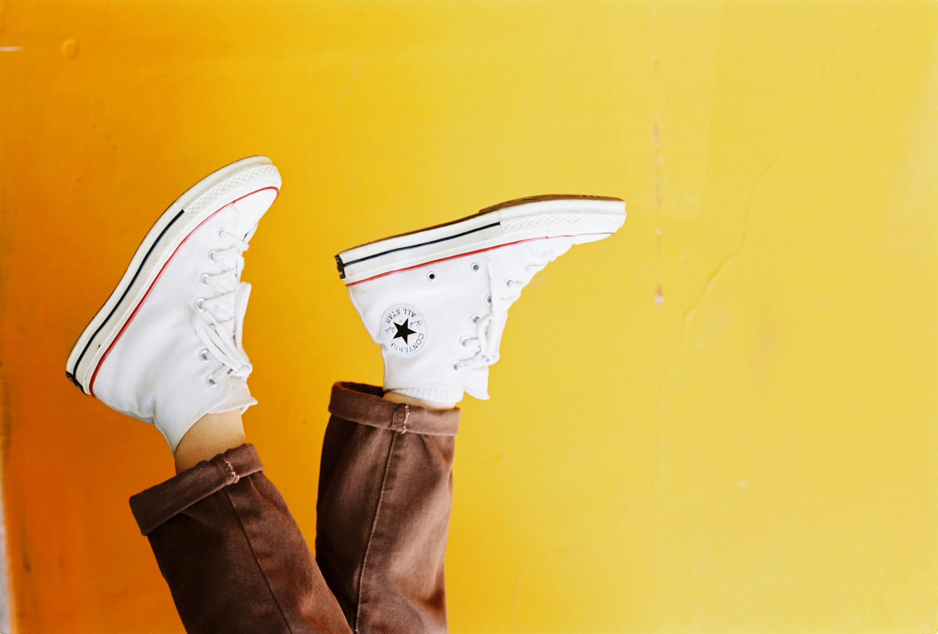 Classic white Converse high-top sneakers, shown against a yellow background.