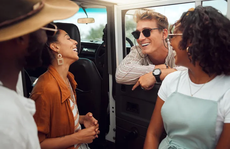 A group of people are hanging out by a truck talking and smiling while wearing sunglasses.