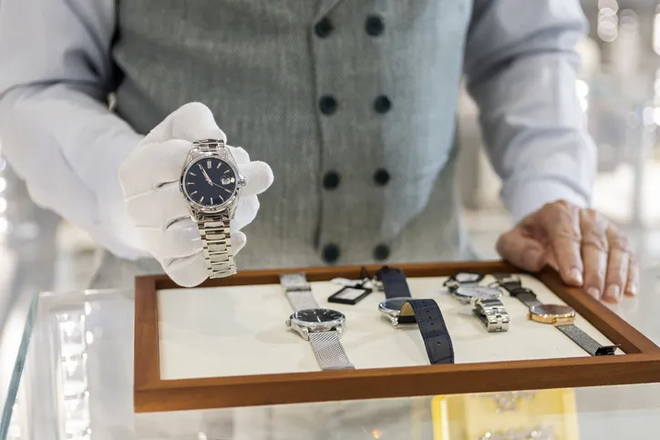 A team member is showcasing a collection of designer watches, wearing white gloves.