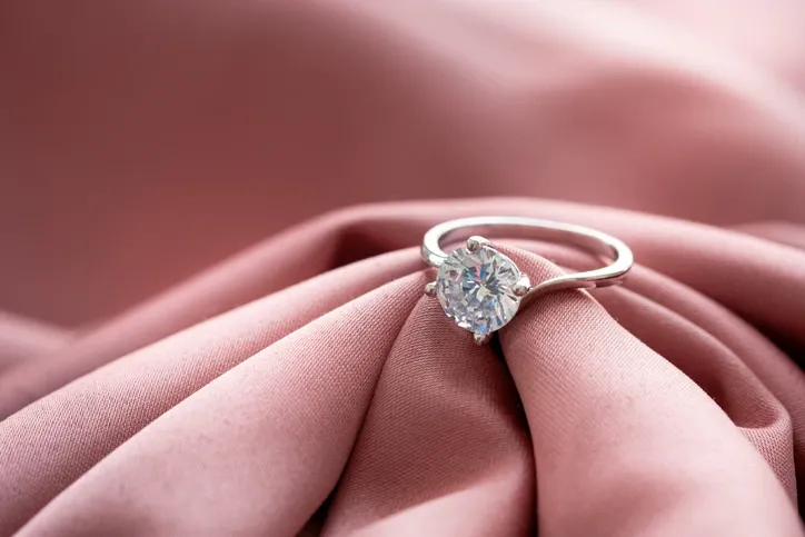 A sparkling diamond ring is sitting on a pink cloth.