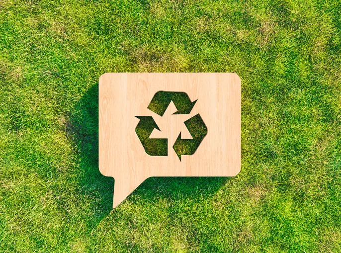 A recycle symbol lays on some green grass.