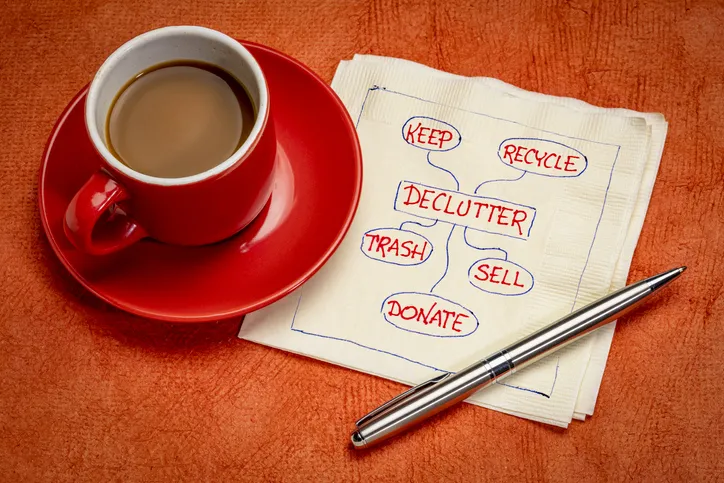 A cup of coffee sits on a saucer which sits on a napkin with handwriting on the napkin. The words “declutter,” “keep,” “recycle,” “trash,” “sell,” and “donate” are all handwritten on the napkin