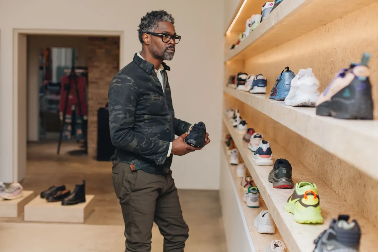 A man is looking at a wall of sneakers at a store while holding one.