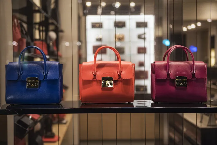 Three luxury handbags sit on a shelf in a store.