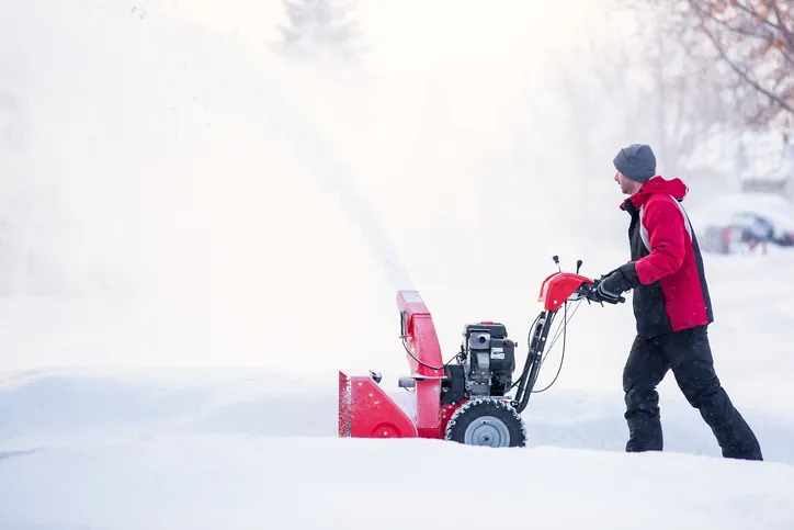 A man is snow blowing his driveway.