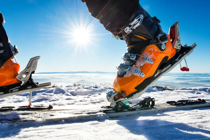 A close up shot of orange ski boots with the sun in the background.