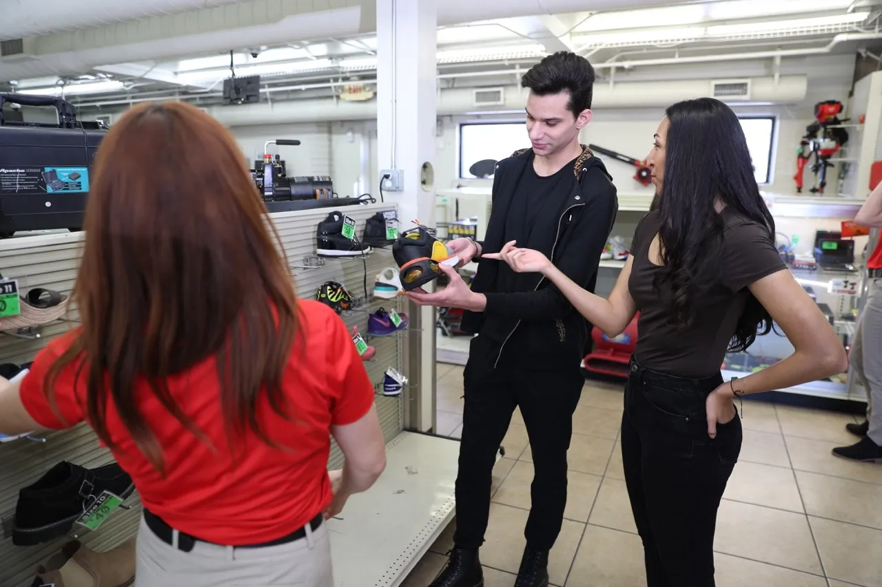 An EZPAWN team member wearing a red shirt is helping a young couple purchase trendy sneakers. A wall of sneakers is in the background.
