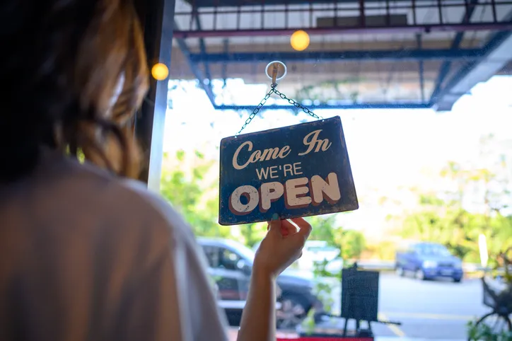 A woman business owner flips the closed sign to open from inside her store