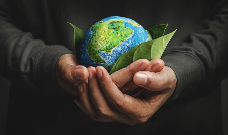 A man is holding a small globe in his hands that sits on a green leaf.