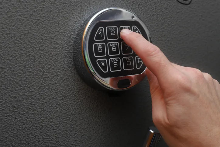 A close-up of a person entering a code on a digital safe keypad, related to firearm storage.