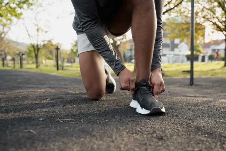 A person kneeling and tying the laces of black sneakers.