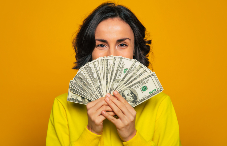 A woman is holding a stack of one-hundred-dollar bills fanned out in from of her mouth.