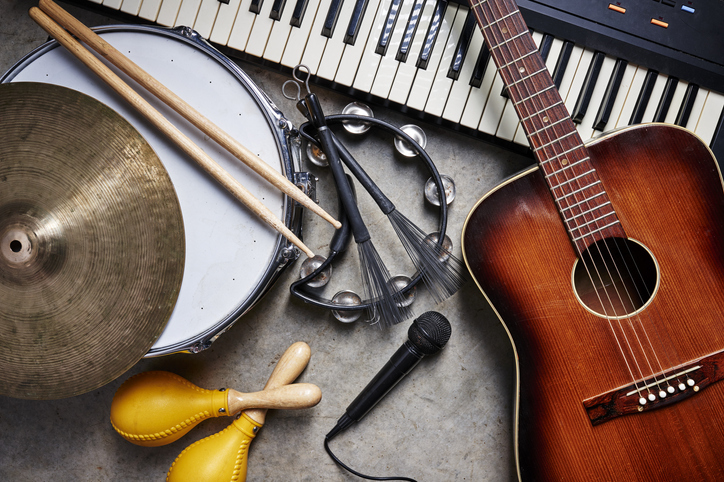 A collection of instruments is lying on the ground: a guitar, piano, drums, tambourine, microphone, etc.