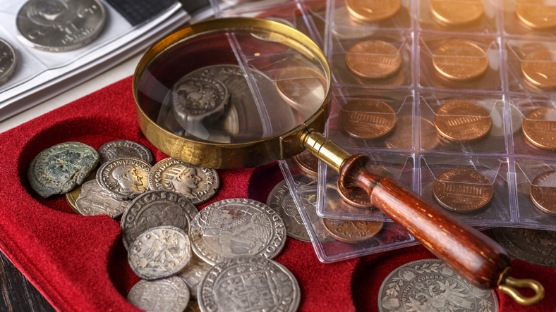 A collection of rare coins is on display while a magnifying glass rests on top of them.