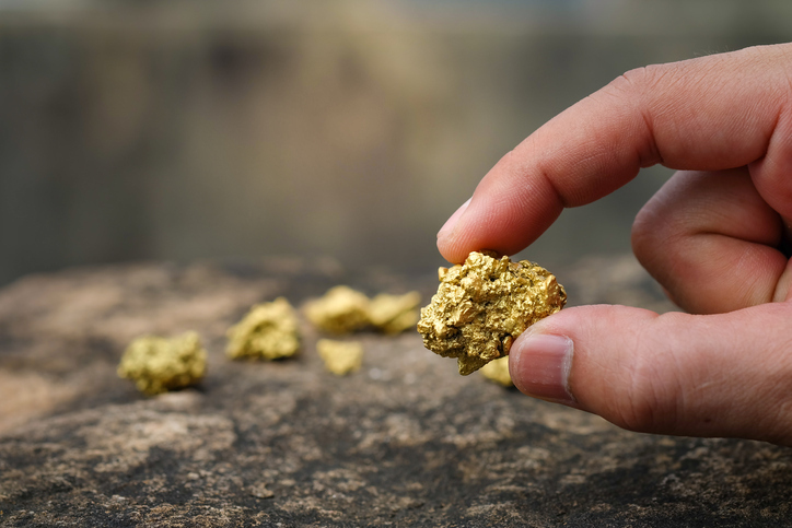 A person is holding a gold nugget with their fingers.