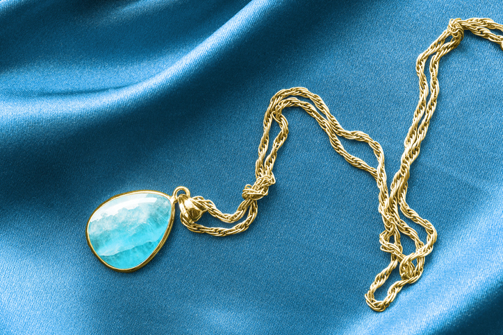 A blue gemstone necklace is laid on a blue cloth.