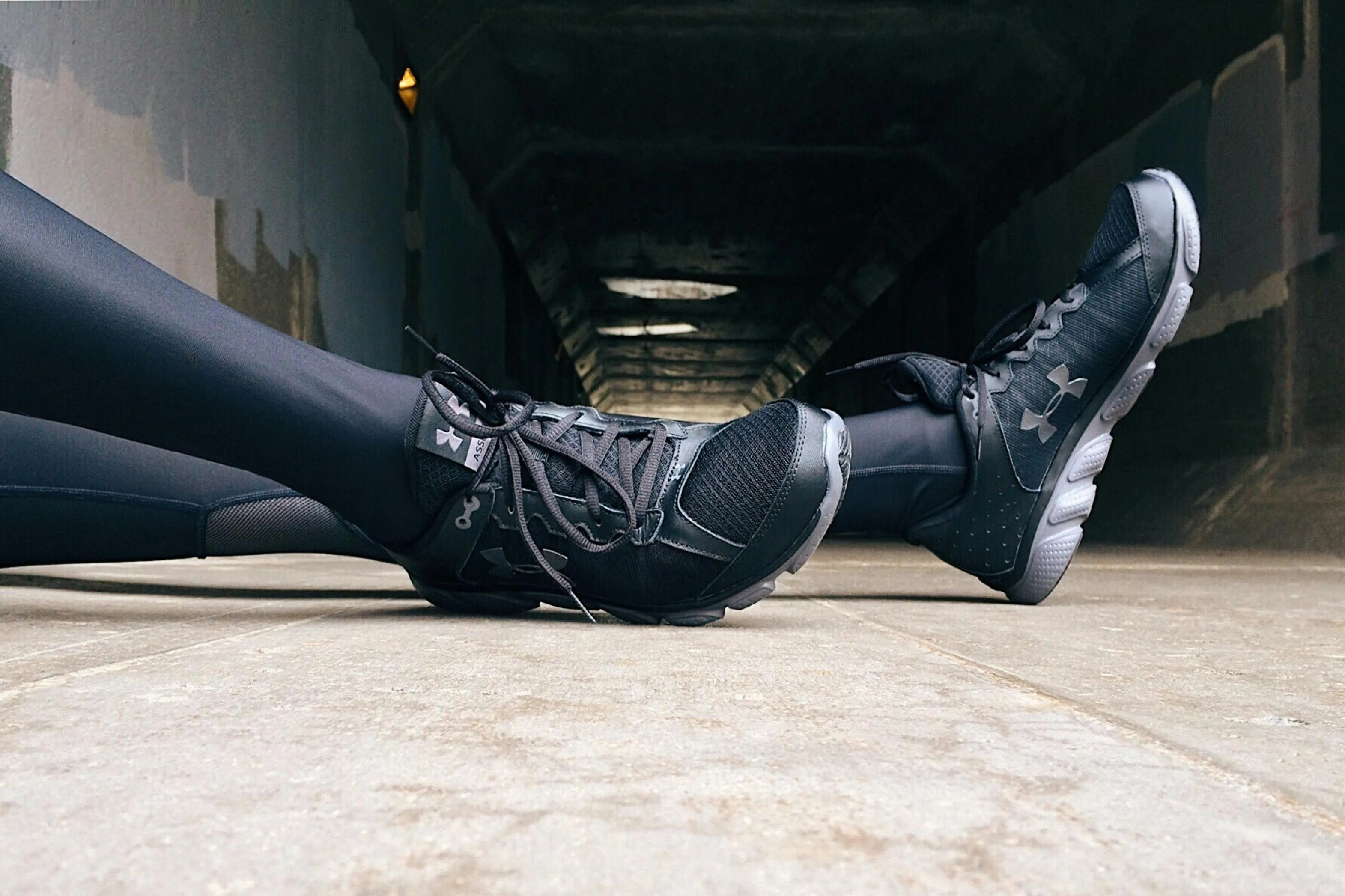 Black Under Armour sneakers, shown in a tunnel-like background.