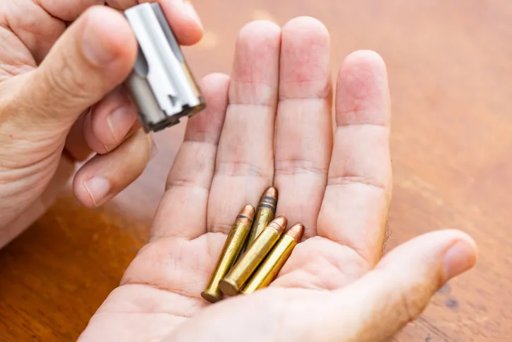 A close-up of a hand holding small ammunition rounds, loading or unloading a firearm.