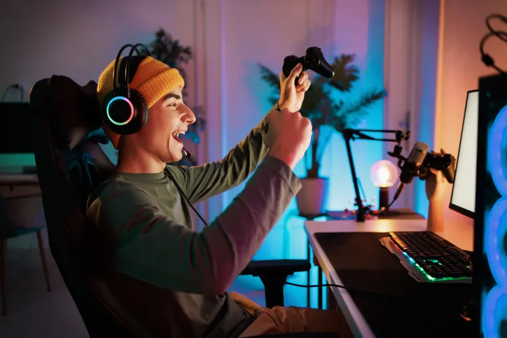 A young man also wearing a headset, celebrating with a controller in hand, suggesting he’s immersed in a gaming experience.