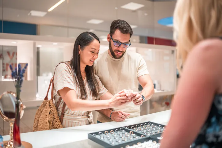 A couple being helped by a store associate while looking at rings in a display case.