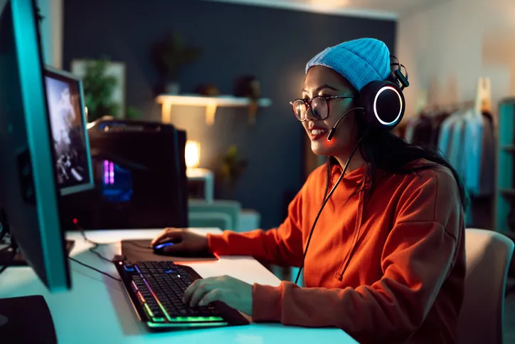 A young woman wearing a headset, seated at a computer, likely gaming or streaming.