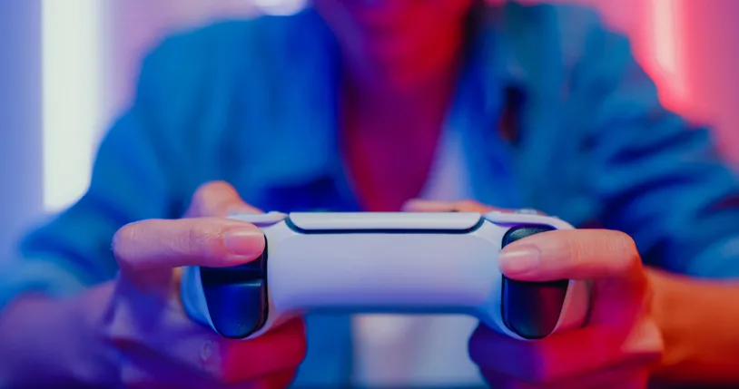 A close-up of a gamer holding a new PlayStation controller with neon lights in the background. His head and legs are out of frame.