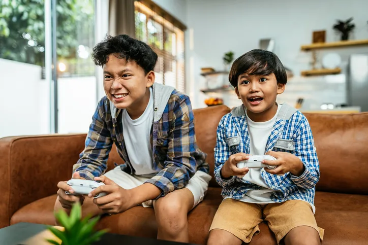 Two children sitting on a couch, actively engaged in a video game, holding controllers and looking focused and excited.