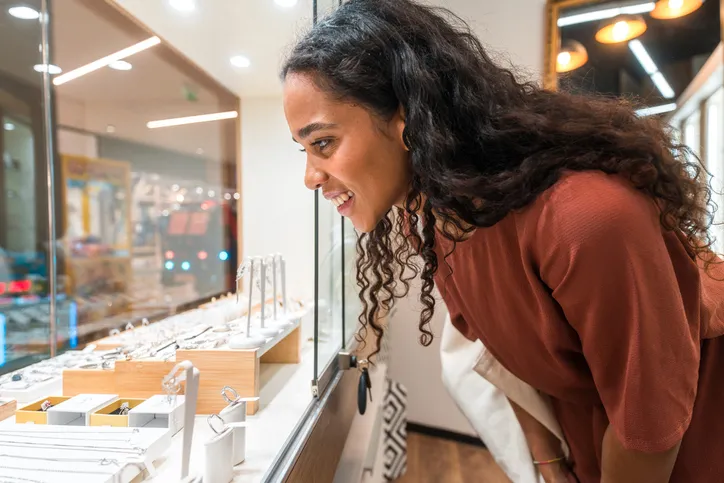 A woman viewing a wide variety of jewelry displayed in a glass case, including rings, necklaces, and bracelets.