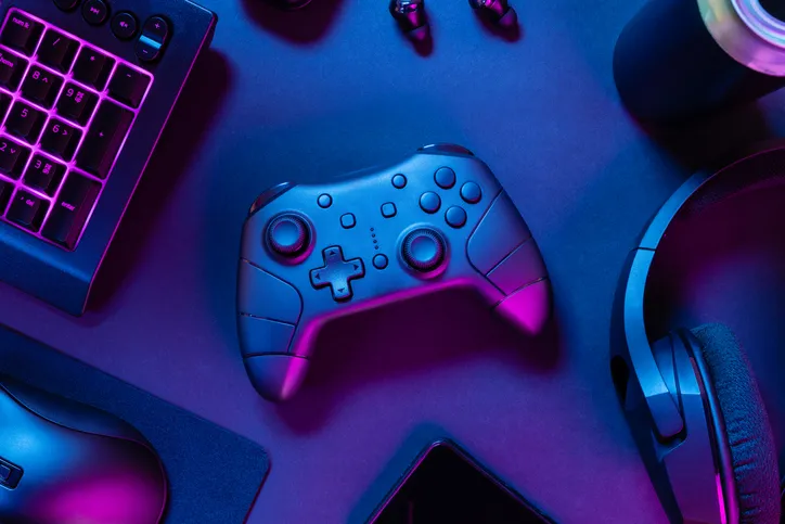 A gaming controller, illuminated in blue and purple lighting, on a desk setup alongside other accessories like a keyboard.