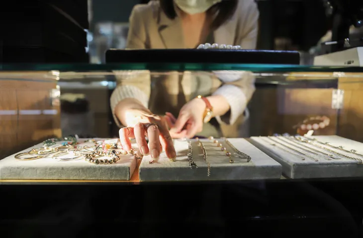 A customer or employee arranging jewelry in a display case, including bracelets and necklaces.