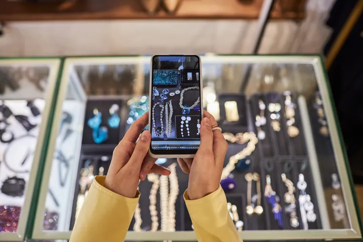 A person taking a picture of jewelry displayed in a case, likely for reference or decision-making.