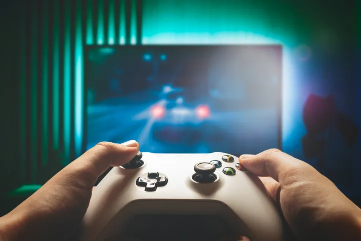 A close-up of hands holding a gaming controller, with a game displayed on a large screen in the background.